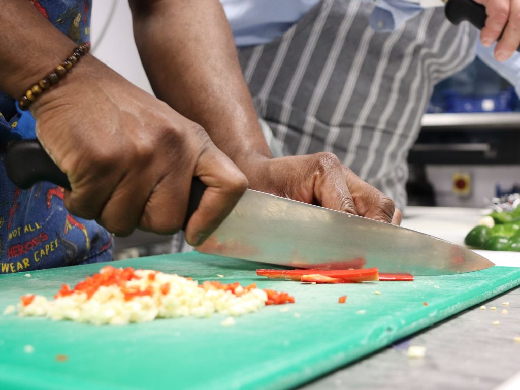 Close up of a person using a chopping board and knife to slice chillies